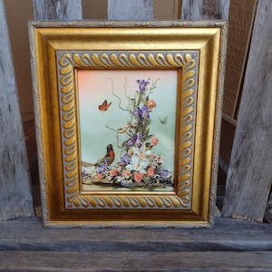 May include: A framed print of a robin perched on a branch with a bouquet of flowers and butterflies. The frame is gold with a decorative border.