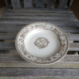May include: A white ceramic soup bowl with a brown floral pattern. The bowl has a scalloped edge and a raised center design.