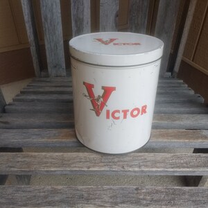 Puede incluir: Lata de metal blanca con una "V" roja y la palabra "VICTOR" impresa en ella. La lata está sobre una superficie de madera.