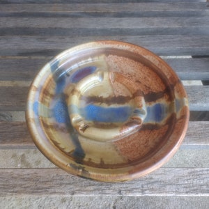 Könnte beinhalten: Ein Aschenbecher aus Keramik mit brauner, blauer und weißer Glasur. Der Aschenbecher hat ein einzigartiges, geschwungenes Design und ist perfekt zum Aufbewahren von Zigaretten.