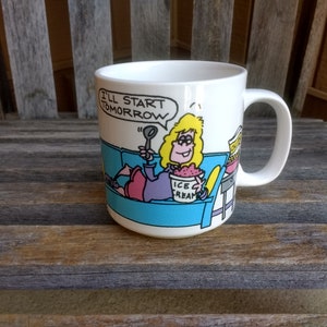 Könnte beinhalten: Weiße Keramik-Kaffeetasse mit einer Cartoon-Illustration einer Frau, die auf einem blauen Sofa sitzt und Eis isst. Der Text "I'll start tomorrow" ist auf die Tasse gedruckt.