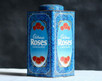Vintage aged storage tin. Cadbury’s ‘Roses’ chocolate box. Tall. Metal container. Sweets. Rusty. Weathered. Circa mid - late 20th century.