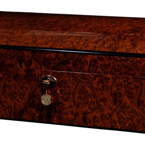 May include: A dark brown wooden humidor with a curved lid and a gold lock and key. The humidor has a black trim around the edges.