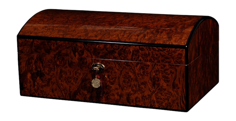 May include: A dark brown wooden humidor with a curved lid and a gold lock and key. The humidor has a black trim around the edges.