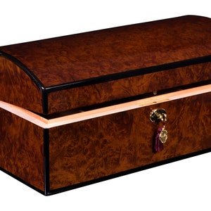 May include: A wooden box with a curved lid, finished in a dark brown wood with black trim. The box has a brass lock and a burgundy tassel.