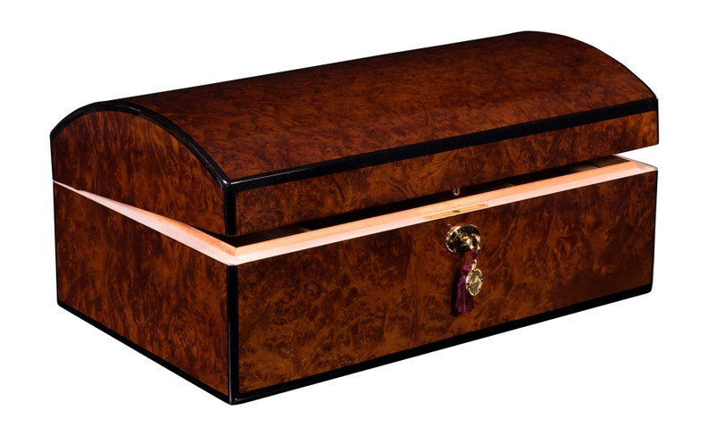 May include: A wooden box with a curved lid, finished in a dark brown wood with black trim. The box has a brass lock and a burgundy tassel.