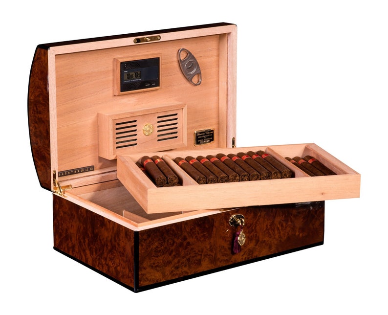 May include: A brown wooden humidor with a hinged lid, open to reveal a cedar-lined interior with a built-in humidifier and a cigar cutter. The humidor is filled with rows of brown cigars.