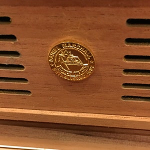 May include: A gold-coloured metal emblem with the text "Daniel Marshall * Family * Established 1982 * NY USA" on a wooden surface.
