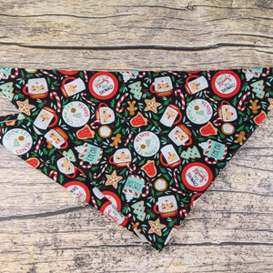 May include: A black bandana with a Christmas-themed print featuring mugs of hot cocoa, cookies, candy canes, and Santa Claus. The print is repeated throughout the bandana.