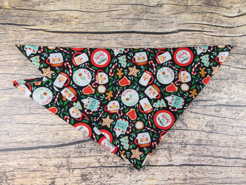 May include: A black bandana with a Christmas-themed print featuring mugs of hot cocoa, cookies, candy canes, and Santa Claus. The print is repeated throughout the bandana.