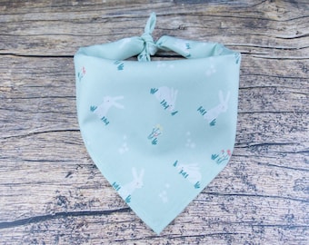 May include: A light blue bandana with a white bunny rabbit pattern. The bandana has a white border and is tied in a knot at the top.