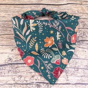 May include: A teal bandana with a floral pattern featuring red, orange, and yellow flowers, green leaves, and gold stars. The bandana is tied in a knot at the top.