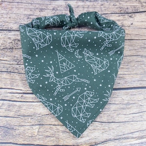 May include: A green bandana with a white geometric pattern of animals and stars. The pattern includes a deer, a wolf, a bear, and a mountain.
