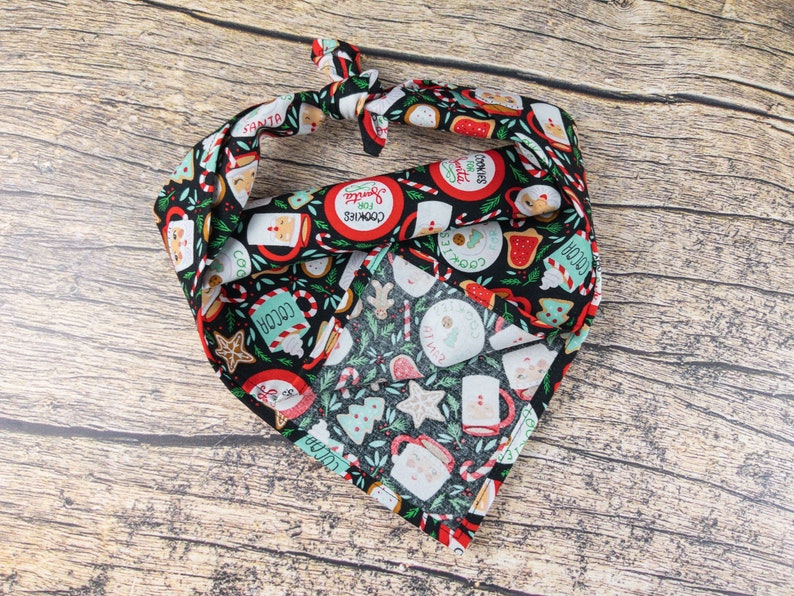 May include: A black bandana with a Christmas-themed print featuring red, green, and white illustrations of cookies, cocoa, candy canes, and other holiday treats. The text "Cookies for Santa" is printed on the bandana.