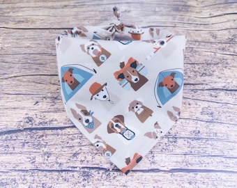 May include: A beige bandana with a pattern of dogs wearing camping gear. The dogs are wearing hats, sunglasses, and backpacks. The bandana has a blue and white tent pattern.