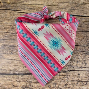 May include: A pink and blue bandana with a geometric pattern. The bandana is tied in a knot and is lying on a wooden surface.