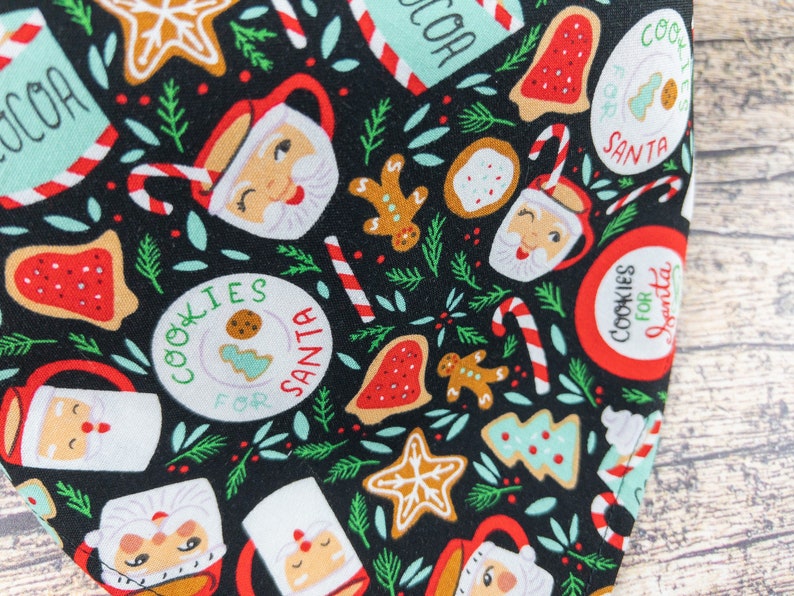 May include: Black fabric with a repeating pattern of Christmas-themed illustrations. The pattern includes gingerbread men, candy canes, cookies, and mugs with Santa's face. The text "Cookies for Santa" is repeated throughout the pattern.