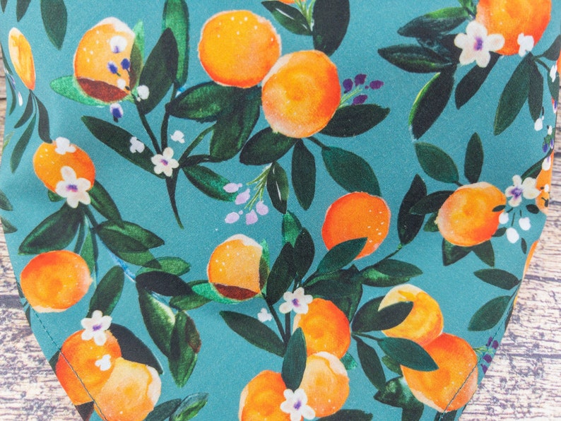 May include: Teal fabric with a repeating pattern of orange citrus fruit and white flowers. The fabric has a watercolor-like design.