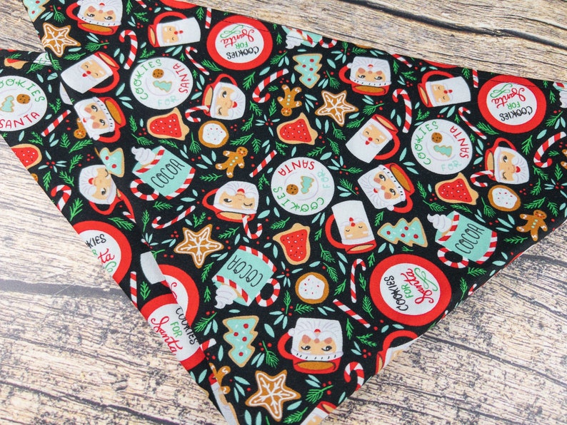 May include: Black fabric with a repeating pattern of Santa Claus mugs, cookies, candy canes, and Christmas trees. The fabric has the text "Cookies for Santa" in a red circle.