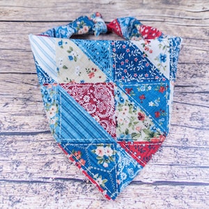 May include: A patchwork dog bandana in shades of blue, red, and white. The bandana features various floral and patterned fabrics, sewn together in a triangular shape. The top has a tie closure for easy wear. A stylish accessory for pets.