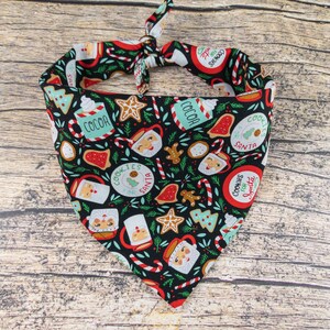 May include: A black bandana with a Christmas theme featuring red, green, and white illustrations of cookies, candy canes, cocoa, and Santa Claus. The bandana has the text "Cookies for Santa" repeated on it.