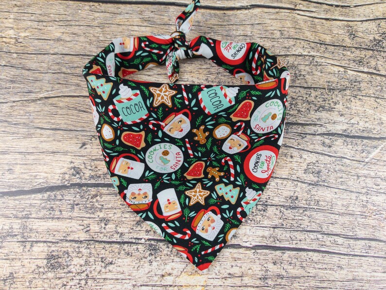 May include: A black bandana with a Christmas theme featuring red, green, and white illustrations of cookies, candy canes, cocoa, and Santa Claus. The bandana has the text "Cookies for Santa" repeated on it.