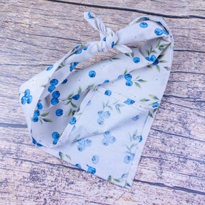 May include: A light blue fabric head wrap with a blueberry and leaf pattern. The head wrap is tied in a knot at the top. The fabric is folded over on itself.