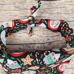 May include: A black bandana with a Christmas-themed print featuring red and green candy canes, gingerbread cookies, and mugs of hot cocoa. The text "Cookies for Santa" is printed on the bandana.