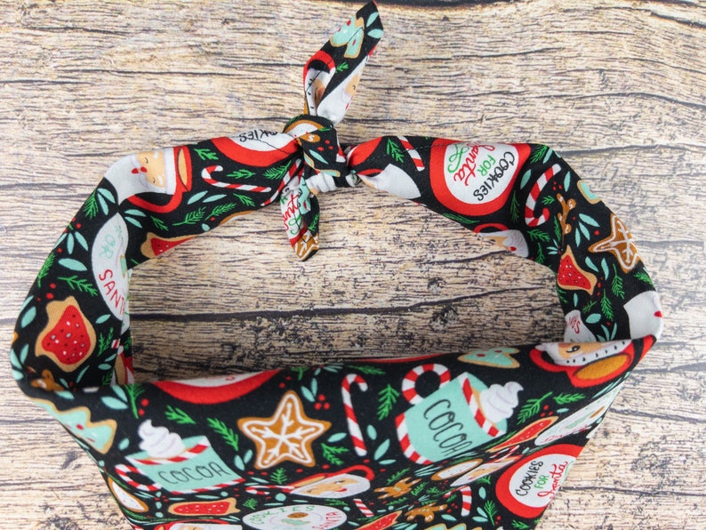 May include: A black bandana with a Christmas-themed print featuring red and green candy canes, gingerbread cookies, and mugs of hot cocoa. The text "Cookies for Santa" is printed on the bandana.