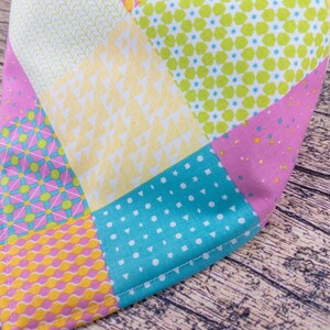 May include: A colorful patchwork fabric with various geometric patterns. The design includes squares and triangles in shades of pink, yellow, turquoise, and green. The fabric is likely cotton or a similar material.