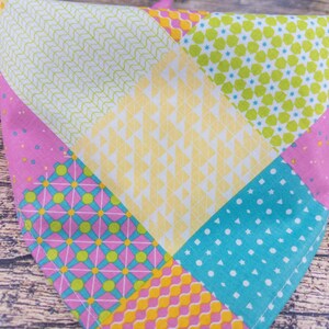 May include: A colorful patchwork bandana featuring various patterns and colors. The bandana is divided into sections of pink, yellow, green, and blue, each with unique designs like polka dots, geometric shapes, and floral patterns. The fabric appears to be cotton.