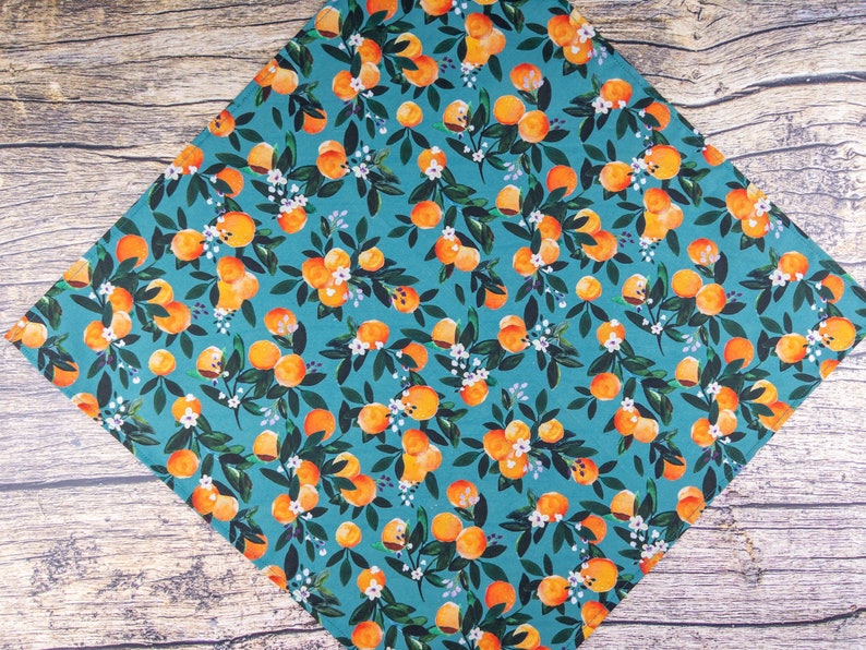 May include: A teal blue fabric with a repeating pattern of orange oranges and white flowers. The fabric is perfect for crafting projects like quilting, sewing, and making accessories.