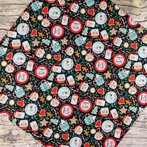 May include: Black fabric with a repeating pattern of Christmas-themed illustrations. The pattern includes cookies, mugs of hot cocoa, candy canes, and stars. The text "Cookies for Santa" is repeated throughout the pattern.