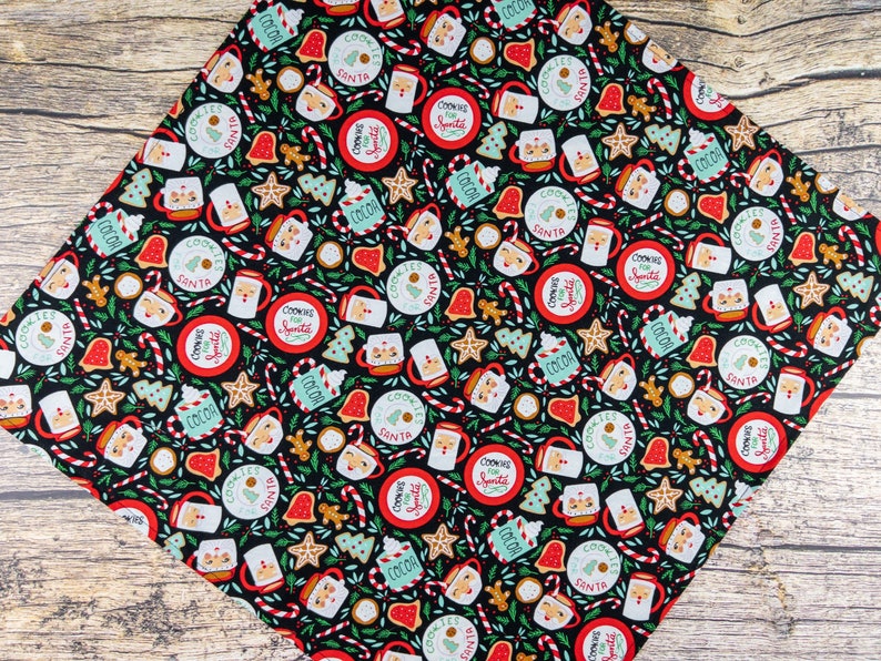 May include: Black fabric with a repeating pattern of Christmas-themed illustrations. The pattern includes cookies, mugs of hot cocoa, candy canes, and stars. The text "Cookies for Santa" is repeated throughout the pattern.