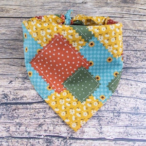 May include: A colorful patchwork bandana with a blue, green, orange, and yellow floral pattern. The bandana is tied in a knot at the top.