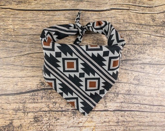 May include: A black and white bandana with a geometric pattern in brown and white. The bandana is tied in a knot and is on a wooden surface.