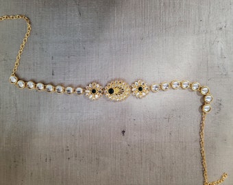 May include: A gold chain necklace with a central design of three round, floral-shaped pendants with black and white stones. The chain is adorned with clear round stones.