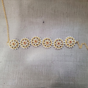May include: A gold necklace with a chain and five round pendants. Each pendant is decorated with white pearls and a red gemstone in the center.