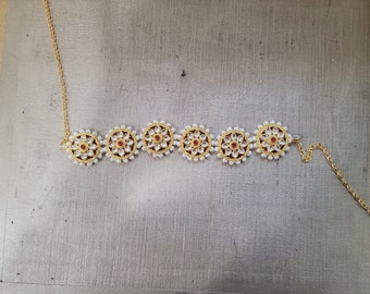 May include: A gold necklace with a chain and five round pendants. Each pendant is decorated with white pearls and a red gemstone in the centre.