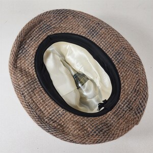 May include: A brown and blue plaid hat with a black brim. The interior is lined with a cream-colored satin fabric. The hat has a classic design, suitable for various occasions.