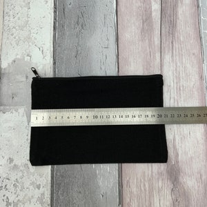 Puede incluir: Una bolsa negra con cremallera con un tirador de cremallera. La bolsa est&aacute; colocada sobre una superficie de madera con una regla que mide 50,8 cm.