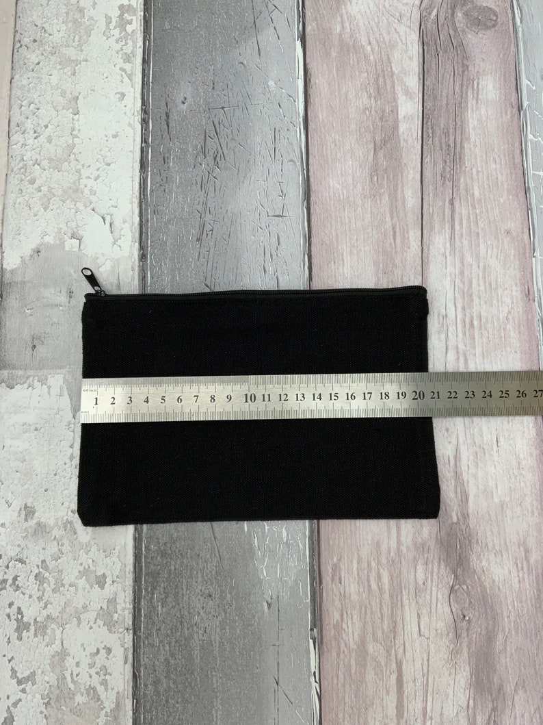 Puede incluir: Una bolsa negra con cremallera con un tirador de cremallera. La bolsa est&aacute; colocada sobre una superficie de madera con una regla que mide 50,8 cm.