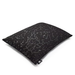 Puede incluir: Una almohada rectangular negra con un patr&oacute;n impreso en blanco de varias constelaciones y estrellas. La tela tiene una apariencia texturizada y una peque&ntilde;a etiqueta de tela negra con el texto blanco PineTales est&aacute; unida a la esquina inferior.