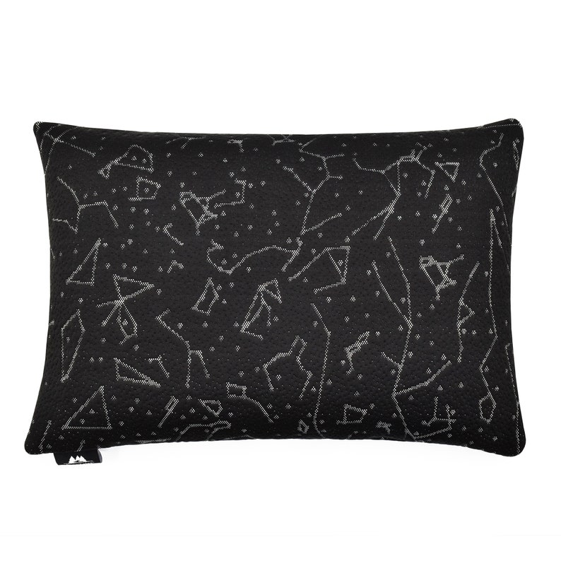 Puede incluir: Un coj&iacute;n rectangular negro con un patr&oacute;n impreso en blanco de varias constelaciones y estrellas en toda la superficie. La tela tiene una apariencia texturizada y una peque&ntilde;a etiqueta negra es visible en la esquina inferior izquierda del coj&iacute;n.