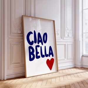 May include: A white framed poster with the words "Ciao Bella" in blue lettering and a red heart in the bottom right corner. The poster is leaning against a white wall with white trim.