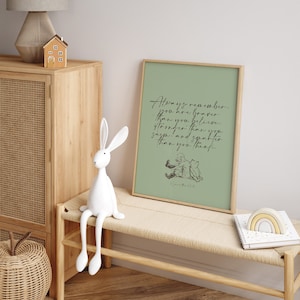 May include: A framed print with a green background and a quote from Winnie the Pooh that reads "Always remember you are braver than you believe, stronger than you seem, and smarter than you think." The quote is in black script font. The print is sitting on a wooden bench with a white rabbit figurine.