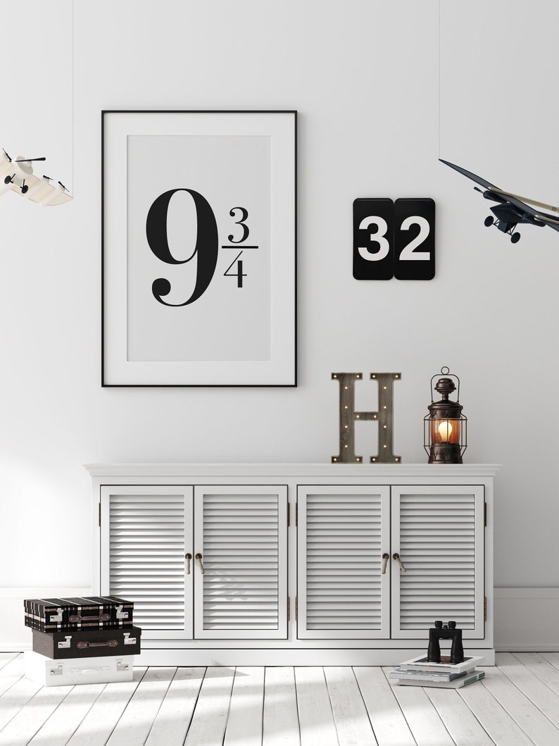 K&ouml;nnte beinhalten: Ein wei&szlig;er Schrank mit drei T&uuml;ren und einem schwarzen gerahmten Druck mit dem Text "9 3/4" an einer wei&szlig;en Wand. Ein schwarz-wei&szlig;er Buchstabe "H" und eine kleine Laterne stehen auf dem Schrank. Zwei Spielzeugflugzeuge h&auml;ngen von der Decke.
