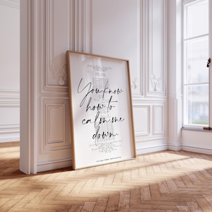 May include: A framed print with the text "You know how to calm me down" in black script. The print is in a light wood frame and leans against a white wall with decorative molding. The room has a hardwood floor and a window.