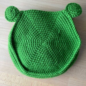 May include: Green crocheted frog-shaped cushion with round ears.