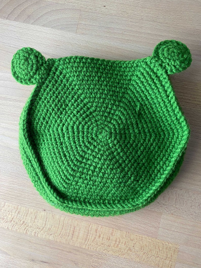 May include: Green crocheted frog-shaped cushion with round ears.